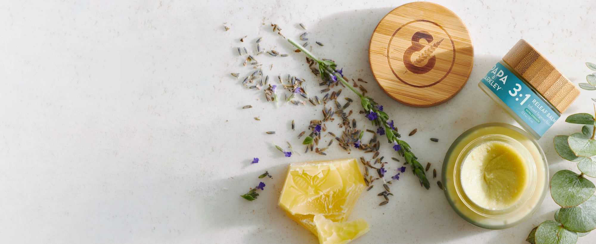 Cosmetic jar with wooden lid, lemon slices, lavender flowers, and eucalyptus leaves on a light background